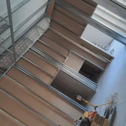 Konstrukcja metalowa pod zabudowę poddasza z płytami karton-gips, widoczny wózek transportowy z narzędziami i materiałami budowlanymi, w tle drabina aluminiowa.