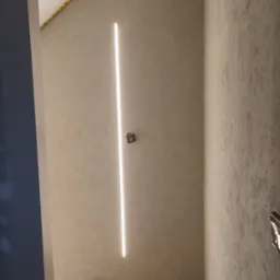 Ściana po nałożeniu gładzi z zamontowanym oświetleniem LED, widoczne zabezpieczenia taśmą malarską przy suficie i podłodze, fragment parkietu.