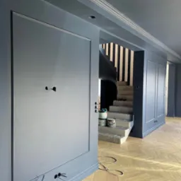 Świeżo pomalowane na szaro ściany z dekoracyjnymi listwami w eleganckim wnętrzu, widoczne puszki z farbą na surowych betonowych schodach z czarno-białymi pasami na ścianie klatki schodowej...