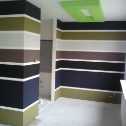 Wnętrze pokoju po malowaniu ścian w poziome pasy o różnych kolorach: oliwkowa zieleń, biel, brąz, czerń i granat. Na suficie widoczny element dekoracyjny w kolorze limonkowym.