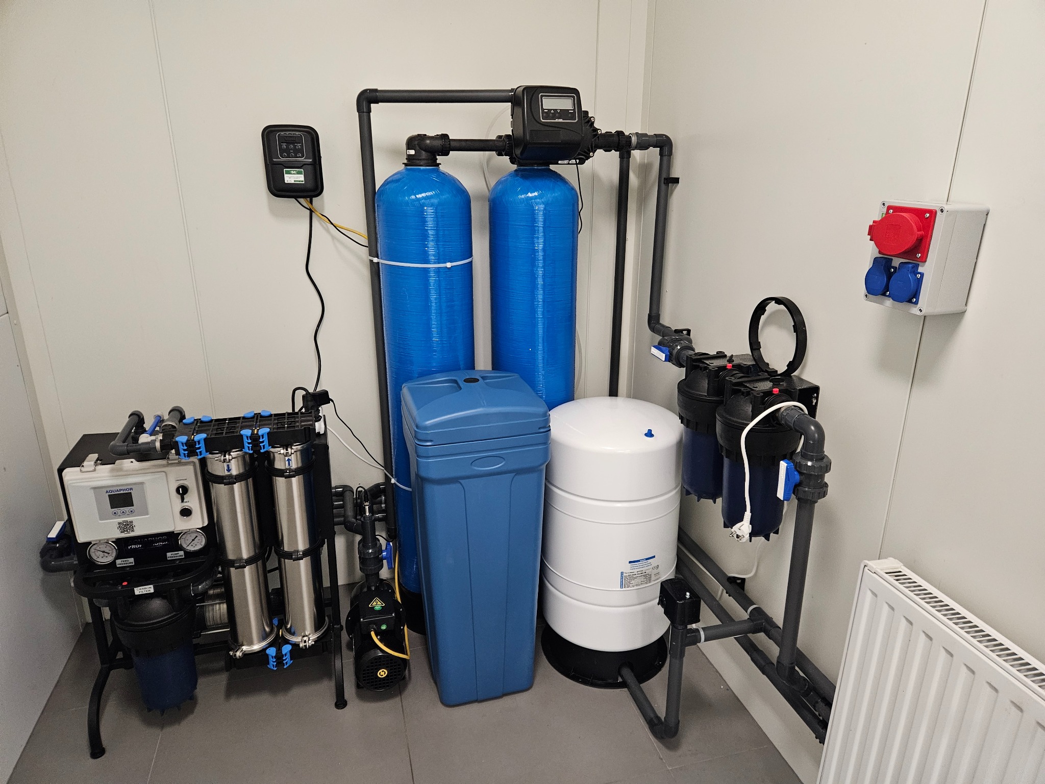 Kompletny system uzdatniania wody z niebieskimi i srebrnymi filtrami, zbiornikami oraz pompą, zainstalowany w pomieszczeniu we Wrocławiu z widoczną instalacją elektryczną i grzejnikiem.