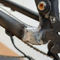 Yauheni Stayukhin - Szczegółowe ujęcie ramy roweru z widocznym spawem w miejscu łączenia elementów, śruby z rdzą i łańcuchem, wskazujące na naprawę lub wzmocnienie konstrukcji.