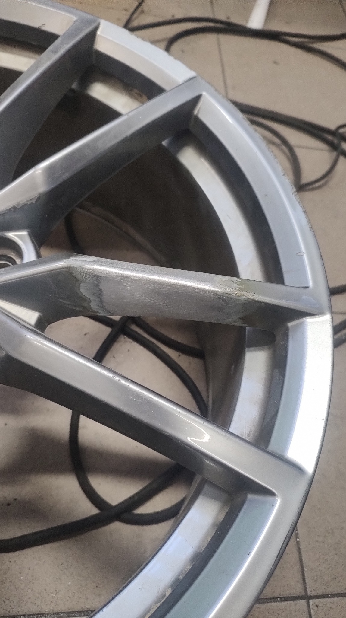 Szlifowana aluminiowa felga samochodowa z widocznymi śladami obróbki i czarnym przewodem w tle.