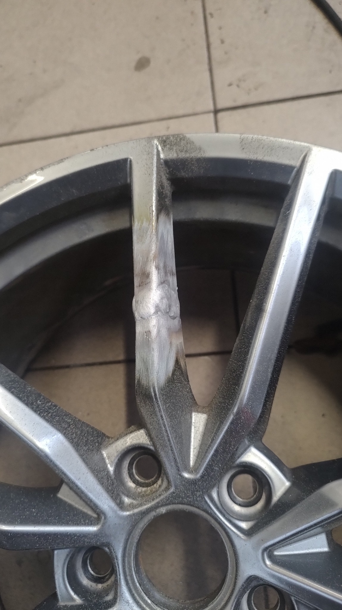 Fragment felgi aluminiowej po naprawie, widoczne ślady szlifowania spoiny w miejscu pęknięcia, przygotowanie do malowania.