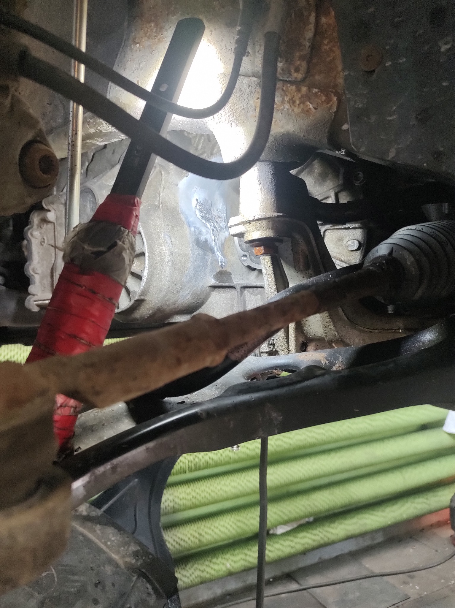 Widok z bliska na spawanie podwozia samochodu z widoczną jarzącą się spoiną, elementami zawieszenia i osprzętem, oświetlone lampą warsztatową