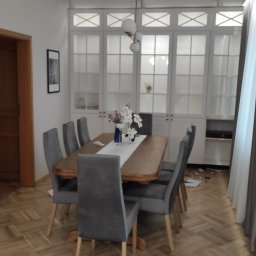 Zbigniew Zagórny - Jadalnia z drewnianym stołem, szarymi krzesłami i zabudową meblową z przeszklonymi frontami w tle.