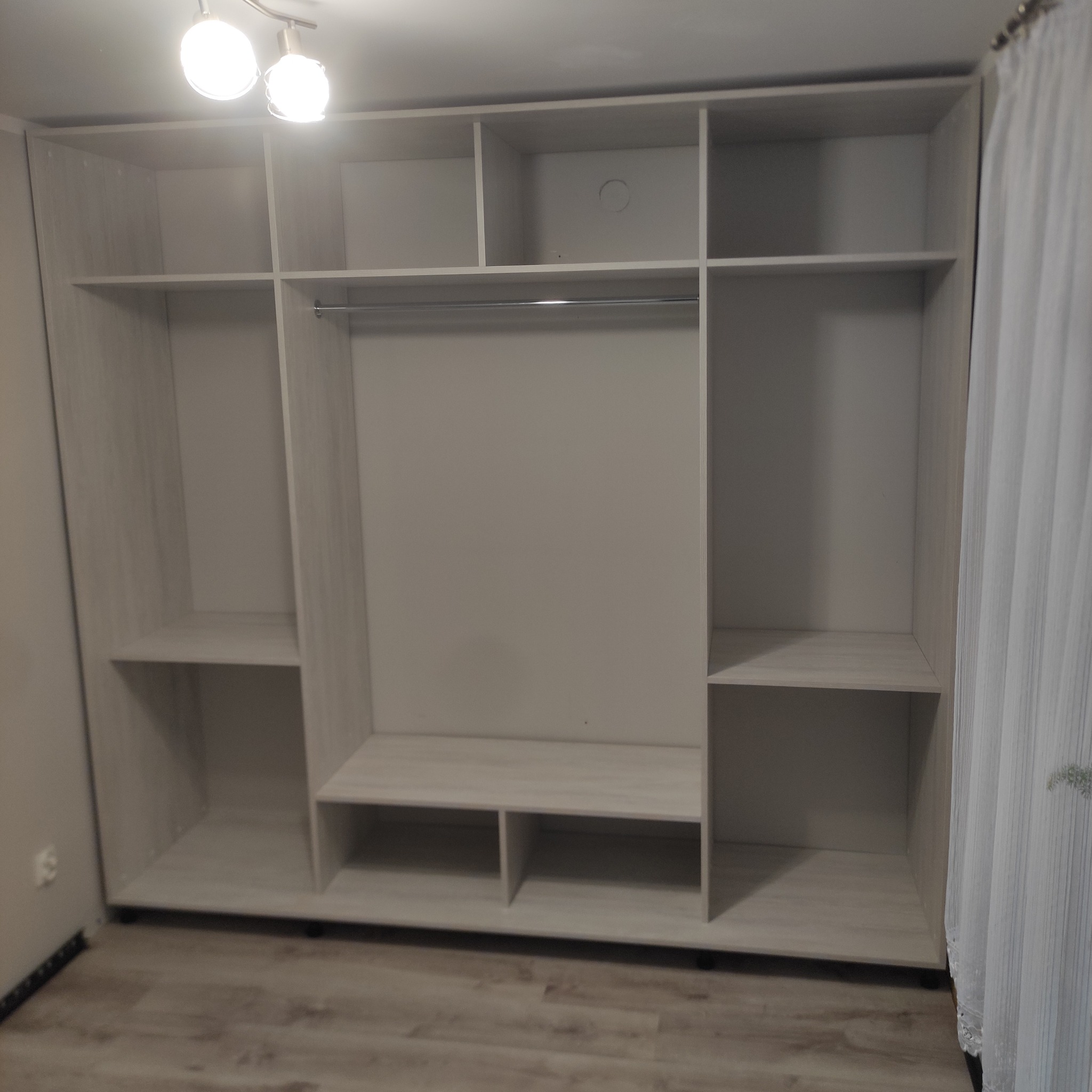 Jasna, duża szafa wnękowa z półkami i drążkiem na ubrania, widoczna na tle ściany i podłogi.