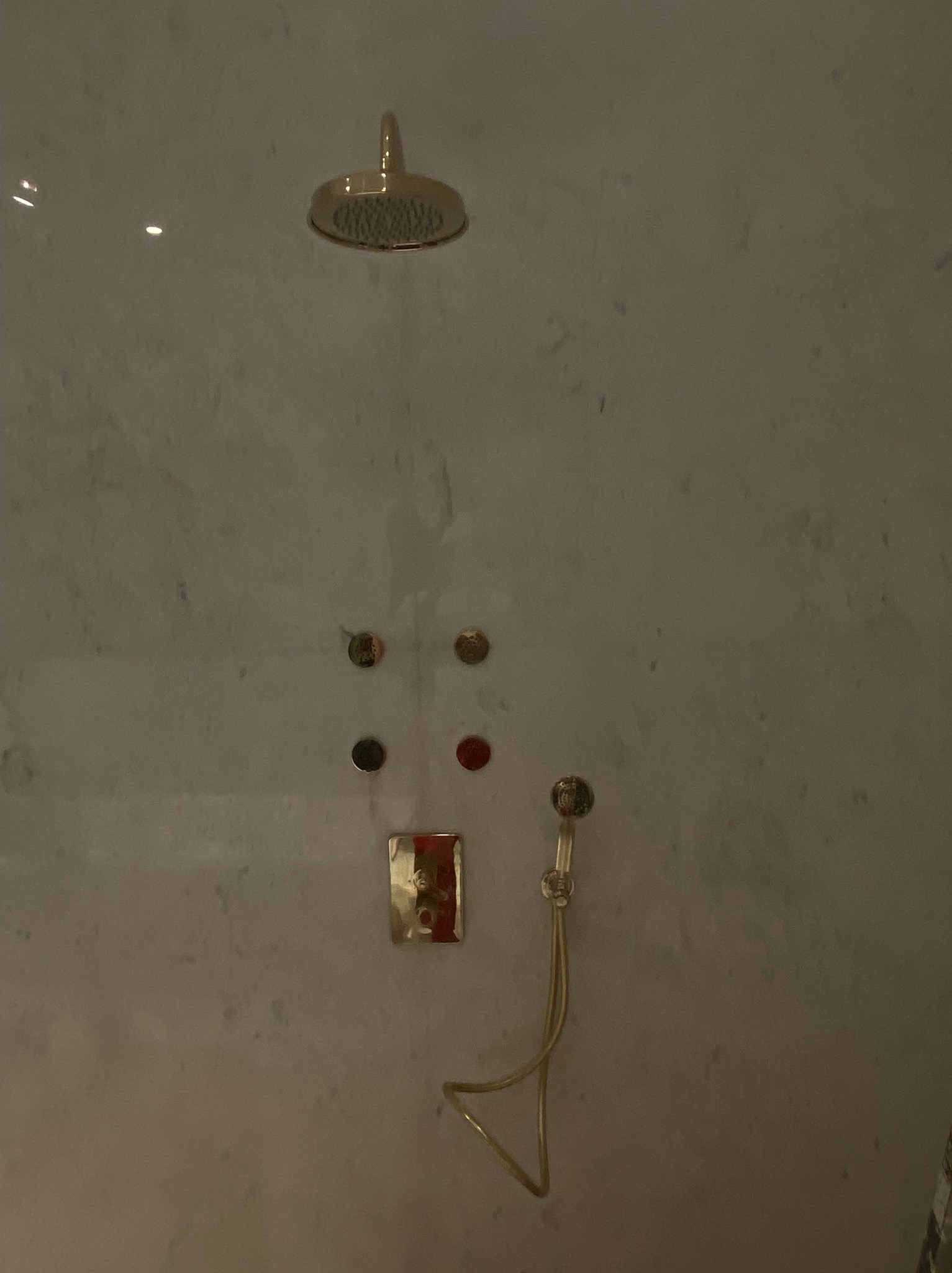 Złota deszczownica, dysze i bateria termostatyczna na marmurowej ścianie w łazience.