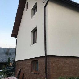 pro Fasada plus - Wykończona elewacja domu jednorodzinnego z brązowym panelem imitującym drewno na dolnej części i jasną, gładką powierzchnią powyżej, widoczne okna i rynna.