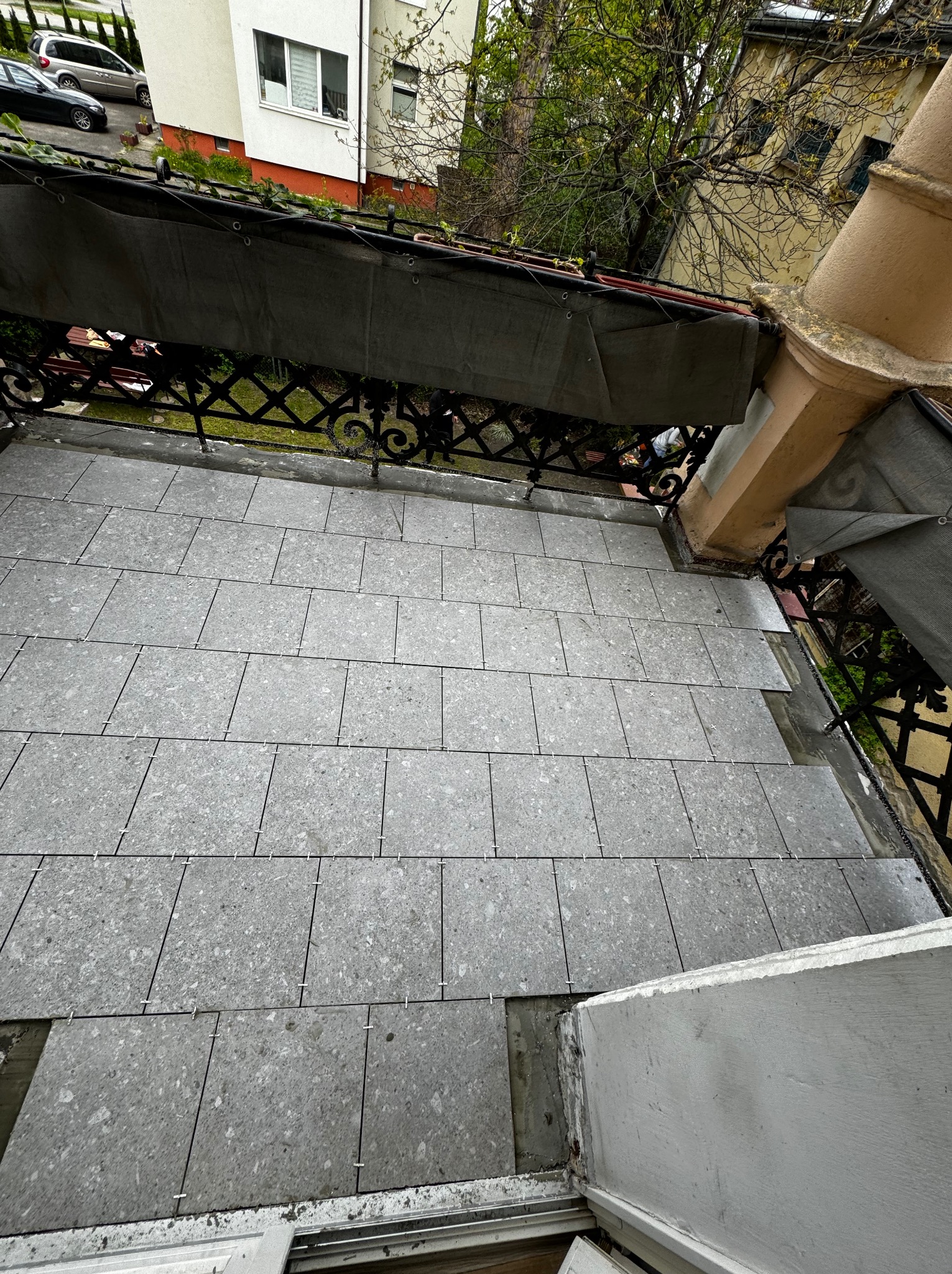 Układanie szarych płytek na balkonie w Gdańsku, widoczne krzyżyki dystansowe, fragment barierki i elewacji budynku.