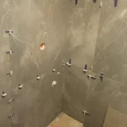 Szare płytki imitujące marmur, ułożone na ścianach łazienki, z widocznymi elementami systemu poziomowania płytek i otworami na instalacje.