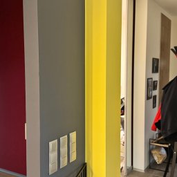 FlexiWorks-Przemysław Wolnik - Fragment wnętrza z pomalowanymi ścianami w kolorach: czerwonym, szarym i żółtym, widoczne włączniki światła oraz balustrada schodów