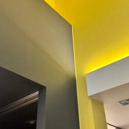 FlexiWorks-Przemysław Wolnik - Fragment wnętrza z pomalowanymi ścianami w odcieniach szarości i intensywnej żółci, z oświetleniem LED w suficie podwieszanym, widok z dołu.