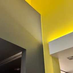 Fragment wnętrza z pomalowanymi ścianami w odcieniach szarości i intensywnej żółci, z oświetleniem LED w suficie podwieszanym, widok z dołu.