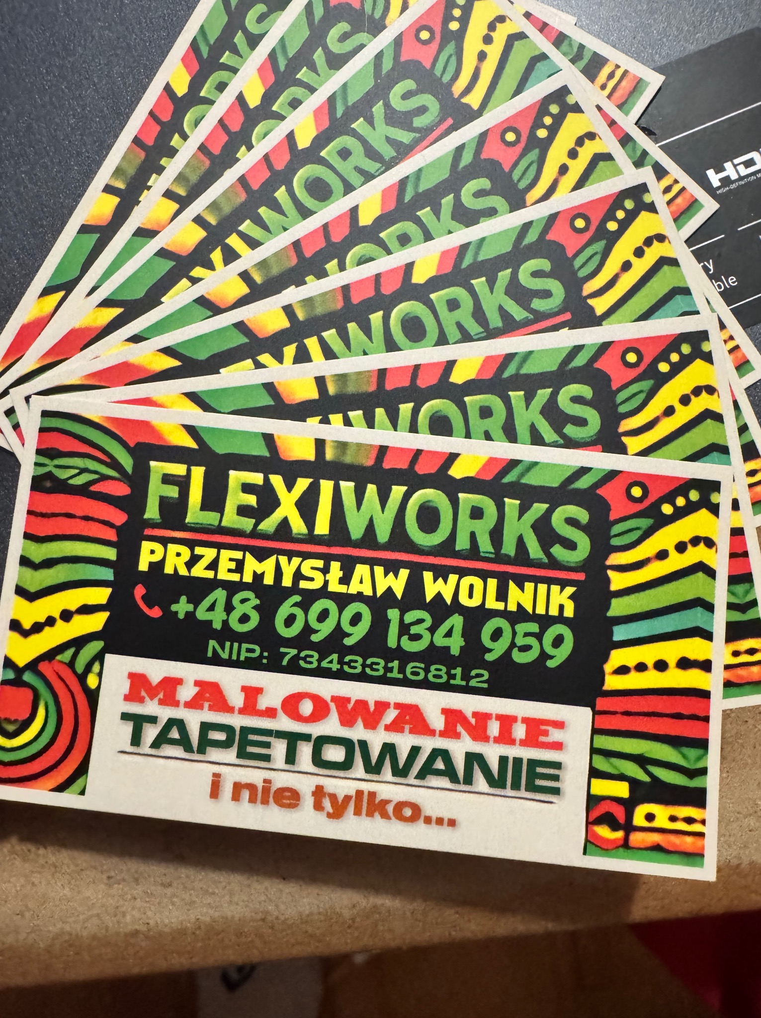 Wizytówki firmy Flexiworks z kolorowym, afrykańskim wzorem, oferującej usługi malowania i tapetowania, z numerem telefonu i NIP.