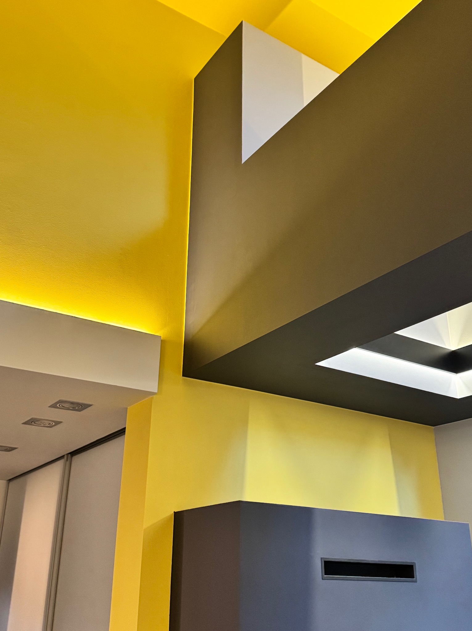 Żółta ściana z ukrytym oświetleniem LED, fragment sufitu z czarną ramą i białym oświetleniem, nowoczesne wykończenie wnętrza.