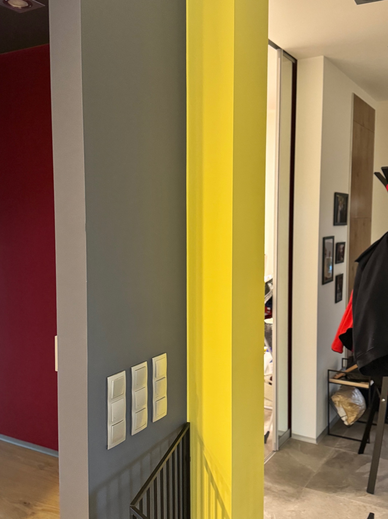 Fragment wnętrza z pomalowanymi ścianami w kolorach: czerwonym, szarym i żółtym, widoczne włączniki światła oraz balustrada schodów