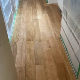 Świeżo ułożona, lakierowana podłoga z paneli drewnopodobnych w jasnym odcieniu dębu, zabezpieczona folią i taśmą malarską przed dalszymi pracami wykończeniowymi.