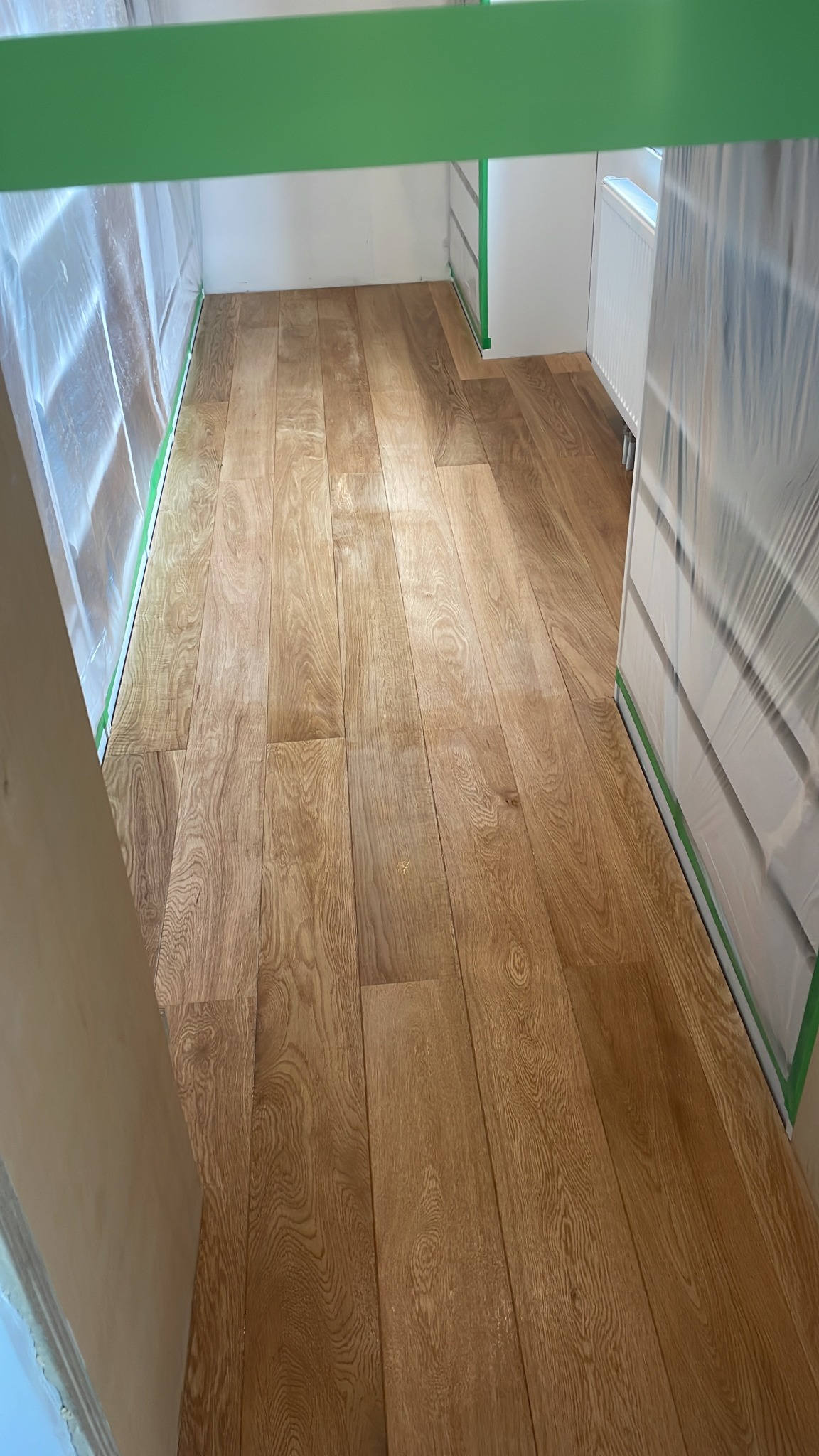 Świeżo ułożona, lakierowana podłoga z paneli drewnopodobnych w jasnym odcieniu dębu, zabezpieczona folią i taśmą malarską przed dalszymi pracami wykończeniowymi.