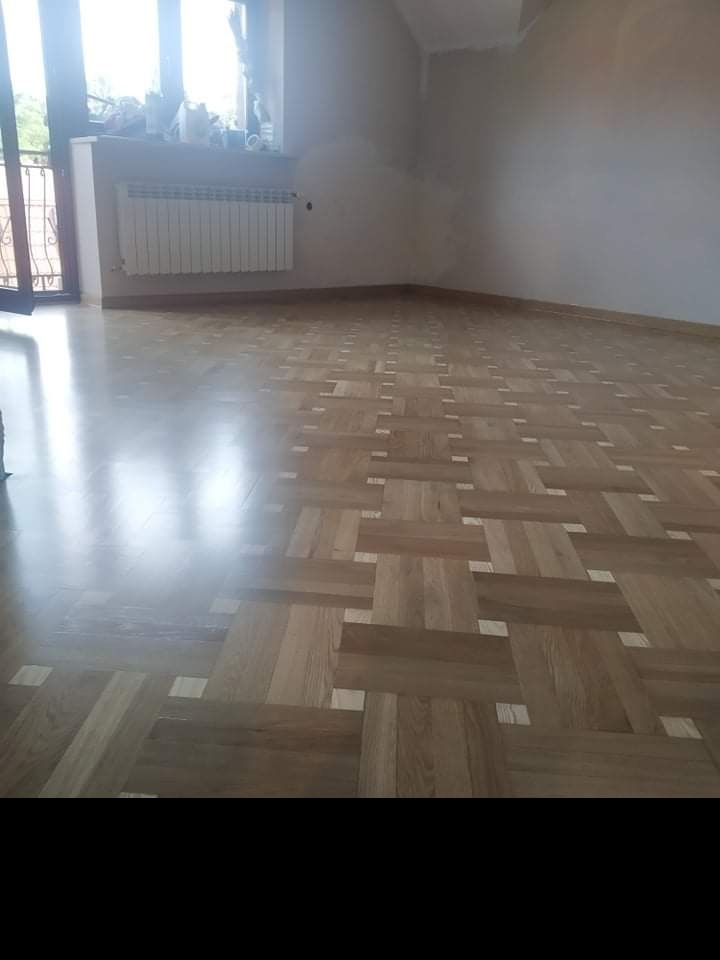 Wzór parkietu ułożonego w jodełkę z jasnymi akcentami, widok na świeżo wykończoną podłogę w pustym pokoju z oknem i grzejnikiem.