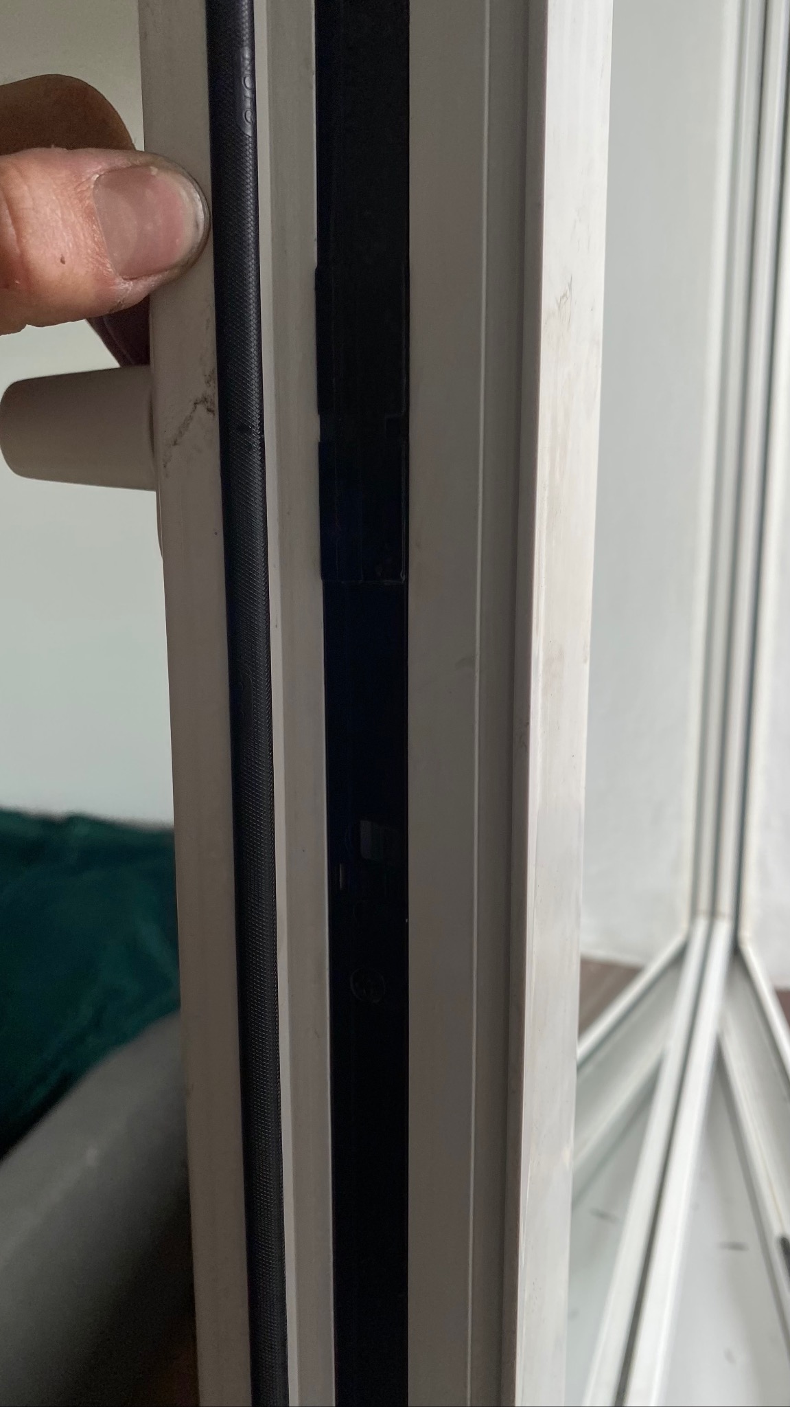 Uszczelka okienna dociskana palcem do ramy, widoczne ślady zabrudzeń na białej ramie okiennej.