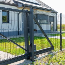 TECHNOMET RAFAŁ KŁOSIŃSKI - Nowoczesna posesja z przesuwną bramą wjazdową i systemem ogrodzenia panelowego w kolorze grafitowym, widok od strony zewnętrznej na tle domu z panelami słonecznymi.
