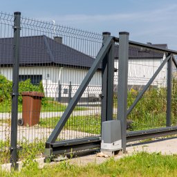 TECHNOMET RAFAŁ KŁOSIŃSKI - Przesuwna brama z metalowej siatki z automatycznym napędem, widoczna na tle domu jednorodzinnego i fragmentu ogrodzenia panelowego.