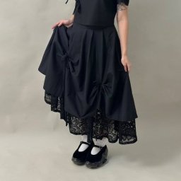 Dom i k sp. z oo - Czarna spódnica z bawełny z koronkowym wykończeniem, zdobiona kokardami, prezentowana na modelce w białych skarpetkach i czarnych butach na platformie.