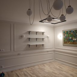 Dom i k sp. z oo - Puste, jasne pomieszczenie z drewnianą podłogą, sztukaterią na ścianach, trzema białymi półkami z czarnymi wspornikami, nowoczesnym oświetleniem sufitowym z okrągłymi kloszami i kwadratową lampą...