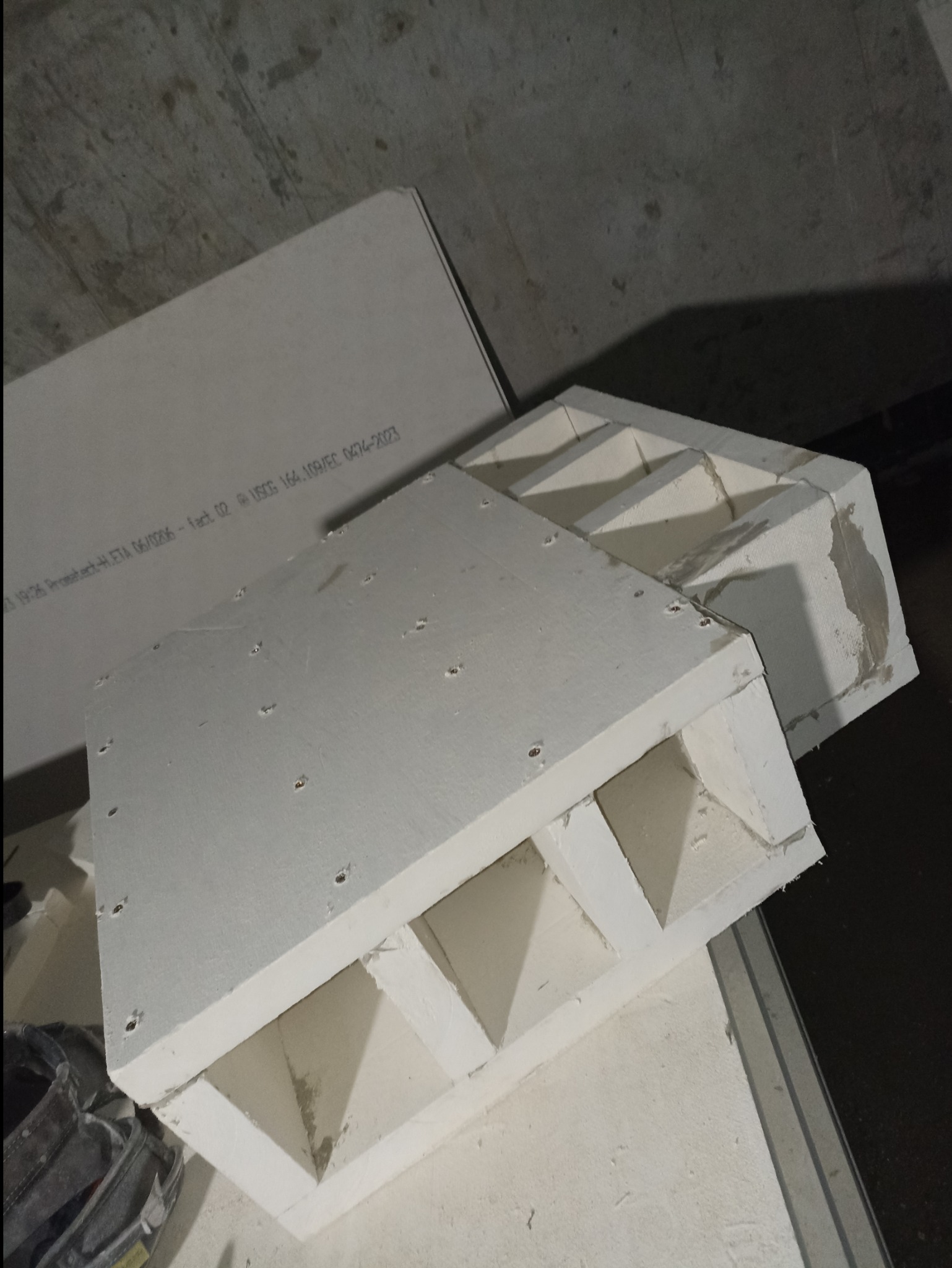 Elementy wentylacyjne z otworami montażowymi i widocznymi spoinami na betonowym tle.