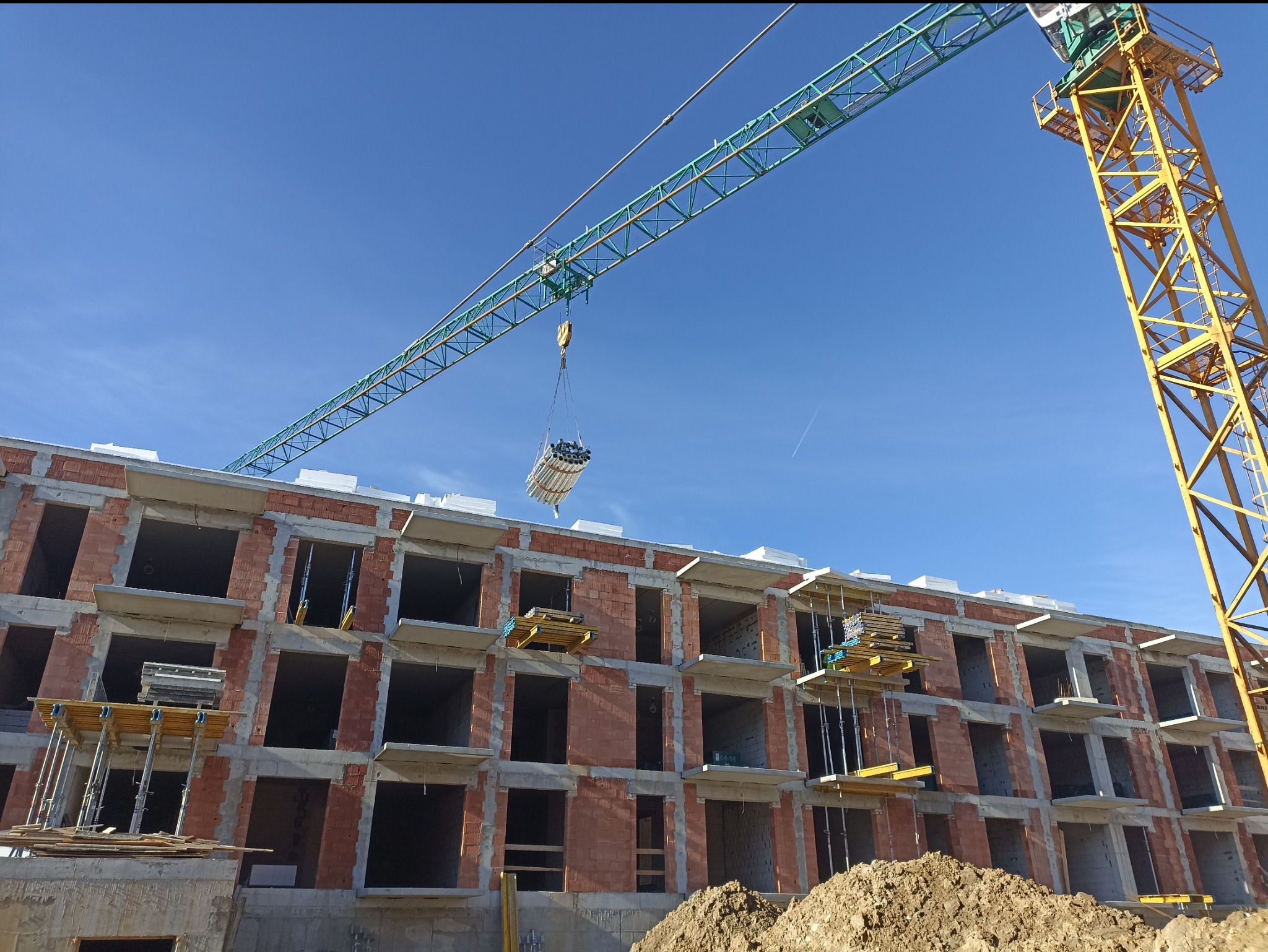 Budynek w stanie surowym otwartym z dźwigiem transportującym materiały budowlane na tle błękitnego nieba.