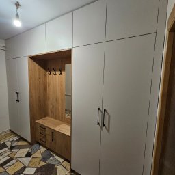 MebleParadise - Jasnoszara szafa wnękowa z drewnianym wykończeniem i lustrem w przedpokoju w Pszczynie. Widoczne czarne, podłużne uchwyty i wzorzysta podłoga.