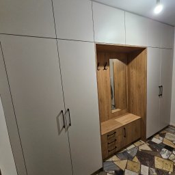 MebleParadise - Nowoczesna szafa wnękowa z drewnianym wykończeniem i wbudowanym siedziskiem, uzupełniona o lustro i wieszaki, na tle wzorzystej podłogi.