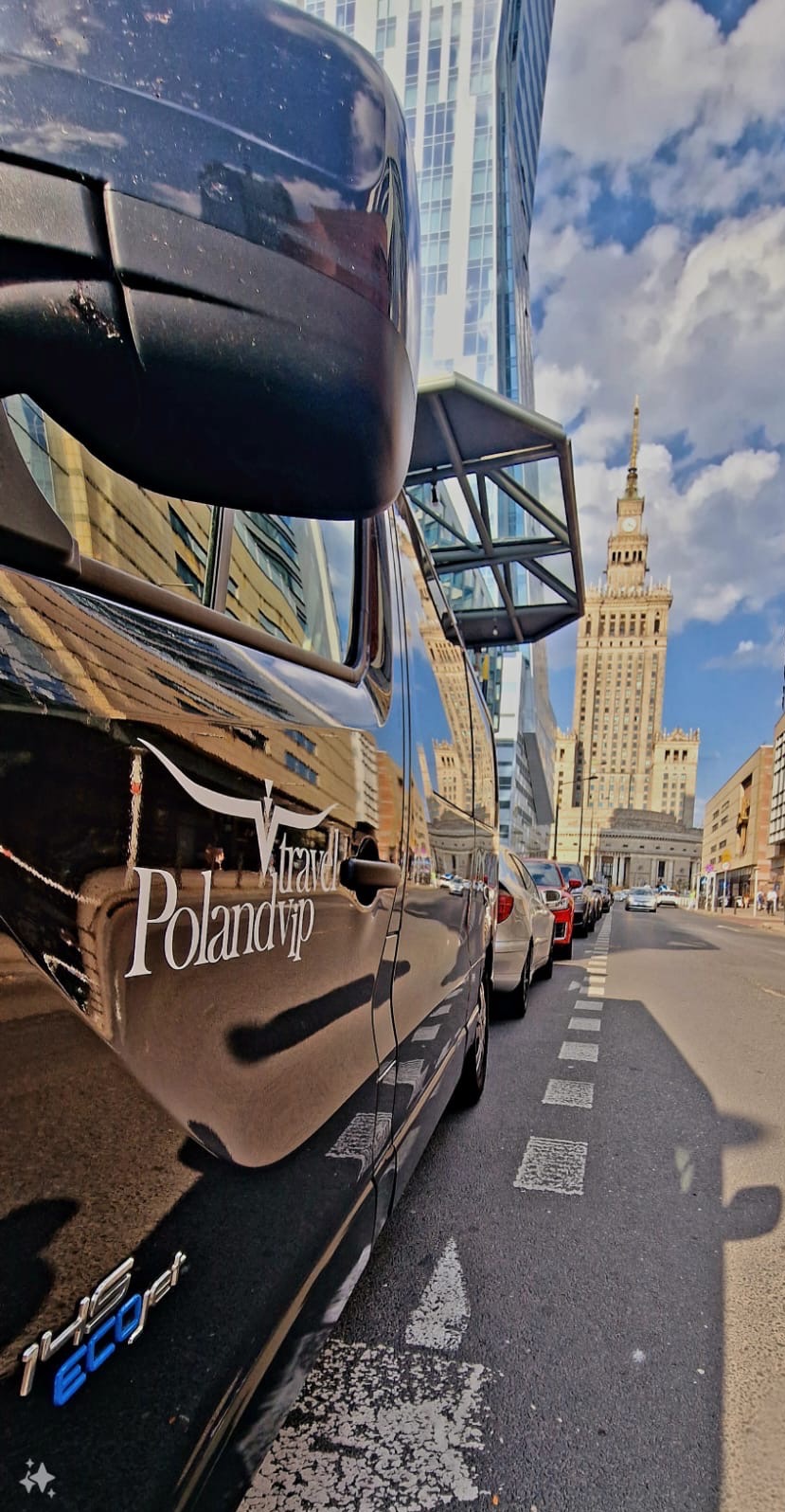 Czarny bus z logo 'Travel Poland vip' zaparkowany na ulicy w Warszawie, w tle Pałac Kultury i Nauki oraz nowoczesne wieżowce.