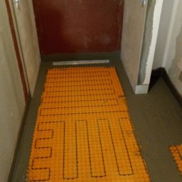 PPHU Jedynka - Pomarańczowa mata grzewcza ułożona na podłodze w trakcie prac wykończeniowych łazienki, widoczne ściany przygotowane do położenia płytek.