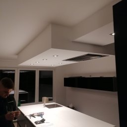 PPHU Jedynka - Montaż oświetlenia podszafkowego w nowoczesnej kuchni z wyspą, widoczny monter przy pracy i narzędzia na blacie.