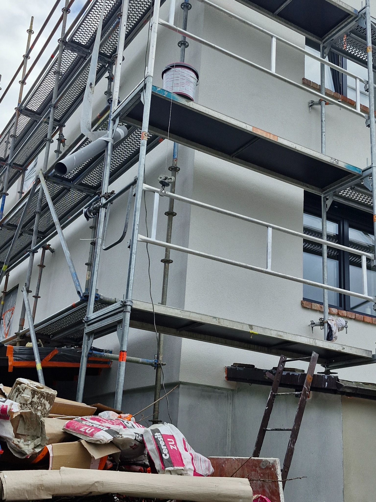 Świeżo otynkowana elewacja budynku w trakcie prac wykończeniowych, widoczna z poziomu rusztowania, z workami po zaprawie w tle.
