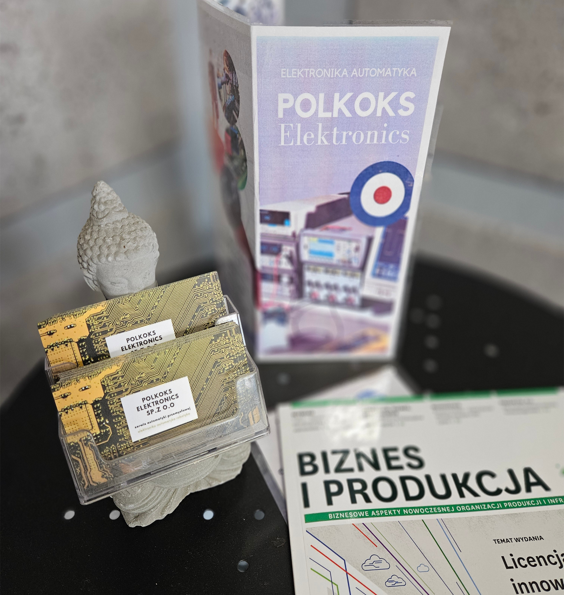 Wizytówki firmy Polkoks Electronics z motywem płyty głównej komputera, ulotka reklamowa i rzeźba głowy Buddy na czarnym tle.