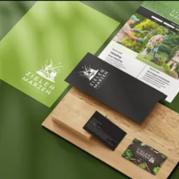 Identyfikacja wizualna firmy Zieleń Marzeń: wizytówki, papier firmowy, font guide prezentujące logo, paletę barw i typografię, ułożone na drewnianym podłożu na zielonym tle.