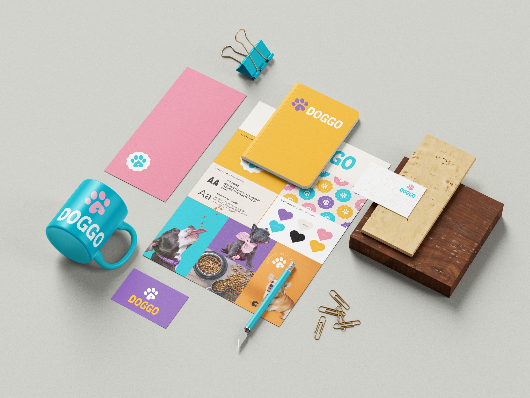 Identyfikacja wizualna marki Doggo: kubek, notatnik, wizytówka, paleta kolorów, kartka, nożyk modelarski, spinacze biurowe i drewniane podstawki prezentowane na jasnoszarym tle.