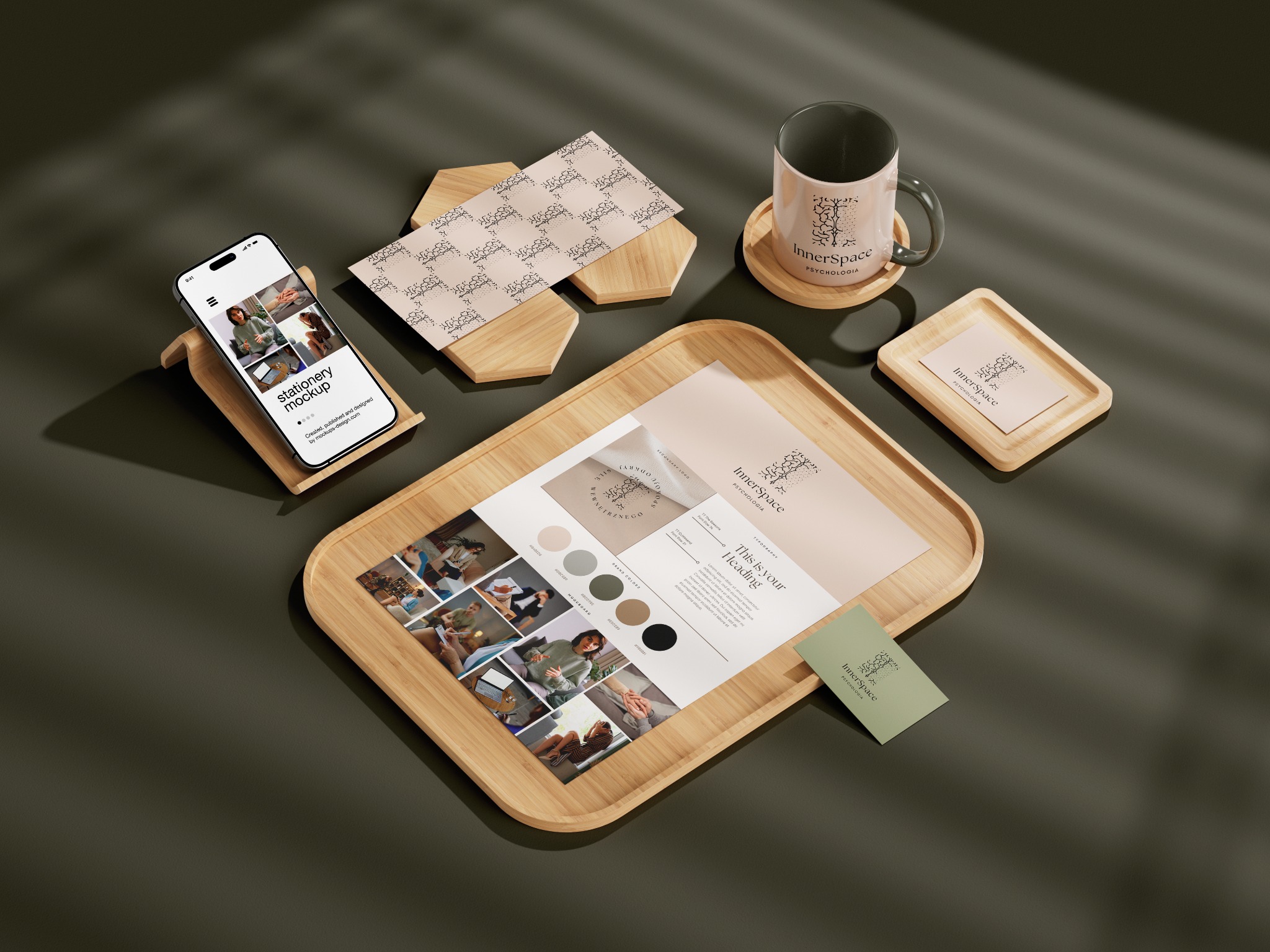 Makieta identyfikacji wizualnej Inner Space z logo na kubku, wizytówkach, papierze firmowym i telefonie, ułożone na drewnianych podstawkach i tacy, oświetlone światłem padającym przez żaluzje.