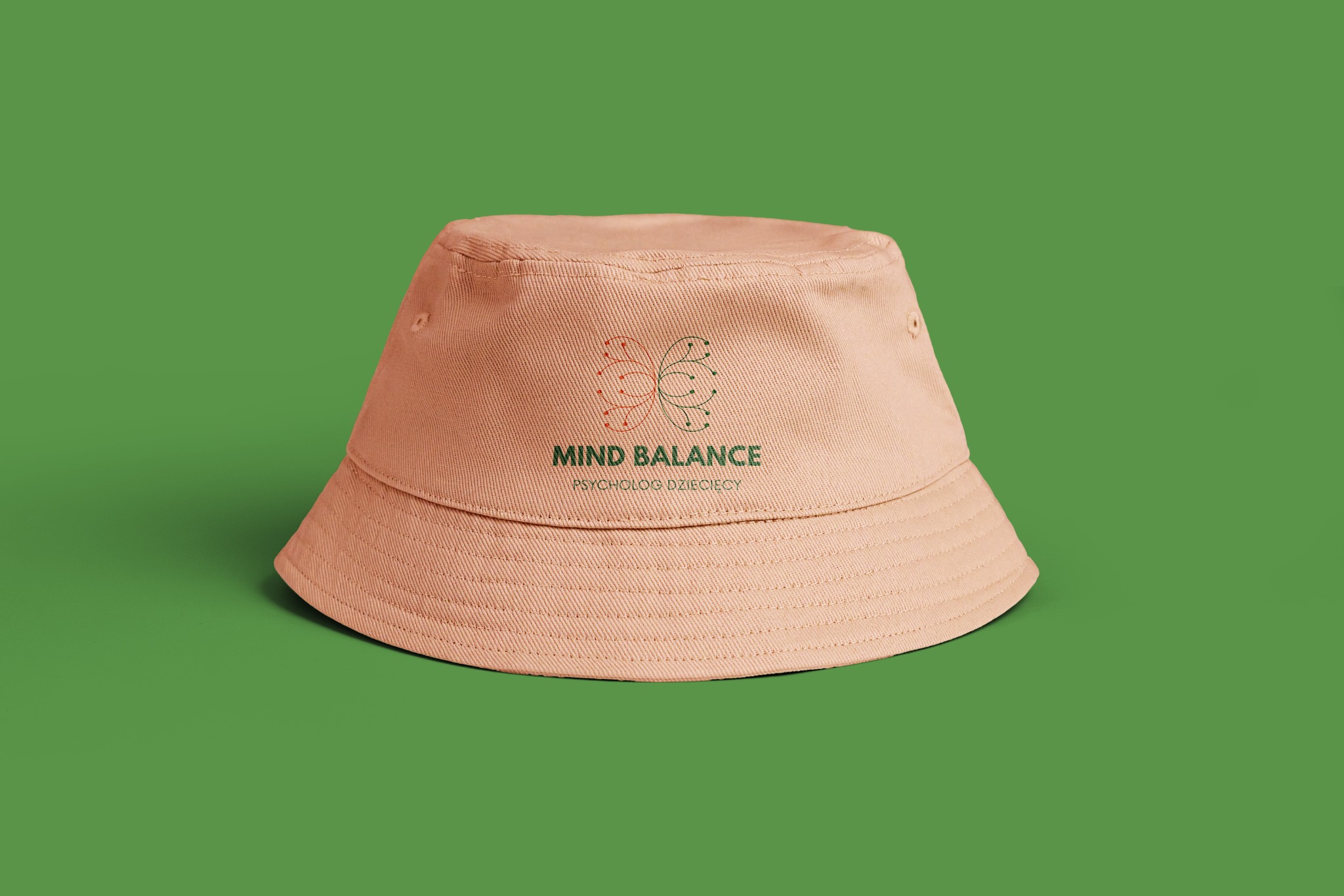 Beżowy kapelusz typu bucket hat z nadrukowanym logo Mind Balance Psycholog Dziecięcy na zielonym tle.