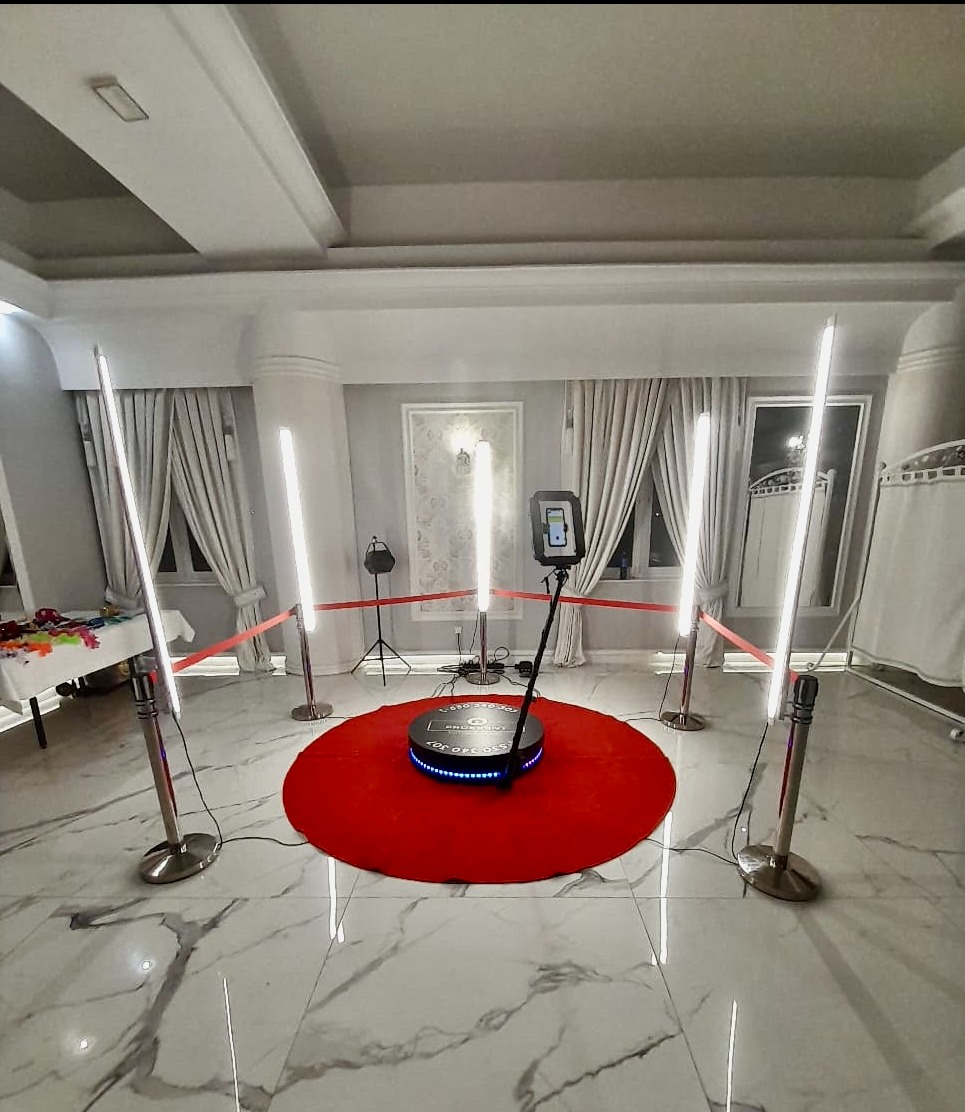 Oświetlona platforma 360 stopni do fotobudki, otoczona czerwonym dywanem i czterema lampami LED na srebrnych statywach w eleganckim wnętrzu z marmurową podłogą.