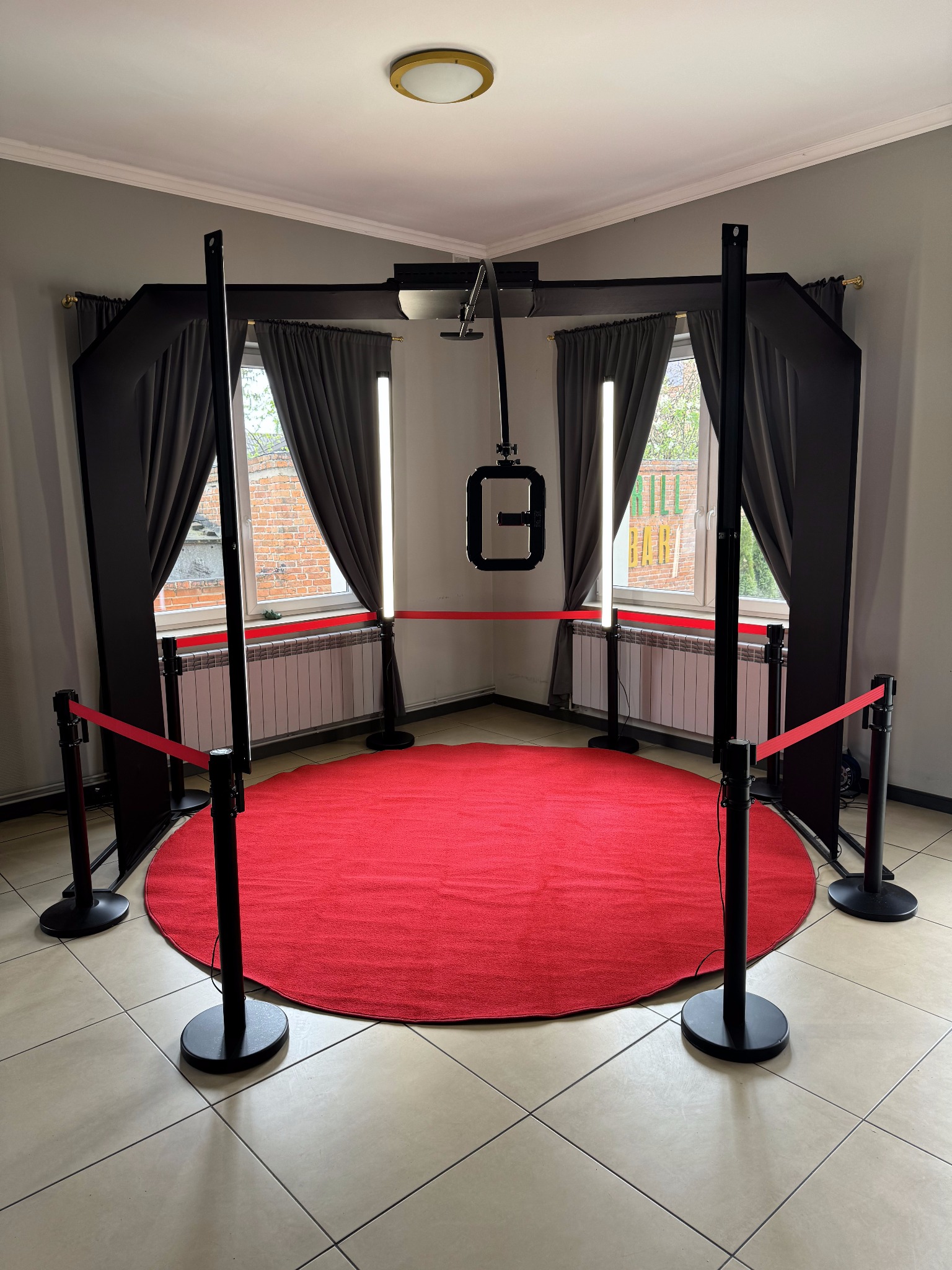 Pusta, profesjonalna przestrzeń do zdjęć z czerwonym okrągłym dywanem, oświetleniem LED i czarnymi zasłonami, oddzielona czerwonymi taśmami.