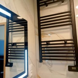 Aqfast - Nowoczesna łazienka z marmurowymi płytkami, czarnym grzejnikiem drabinkowym i lustrem z podświetleniem LED.