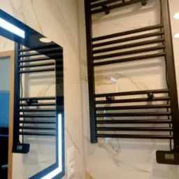 Nowoczesna łazienka z marmurowymi płytkami, czarnym grzejnikiem drabinkowym i lustrem z podświetleniem LED.