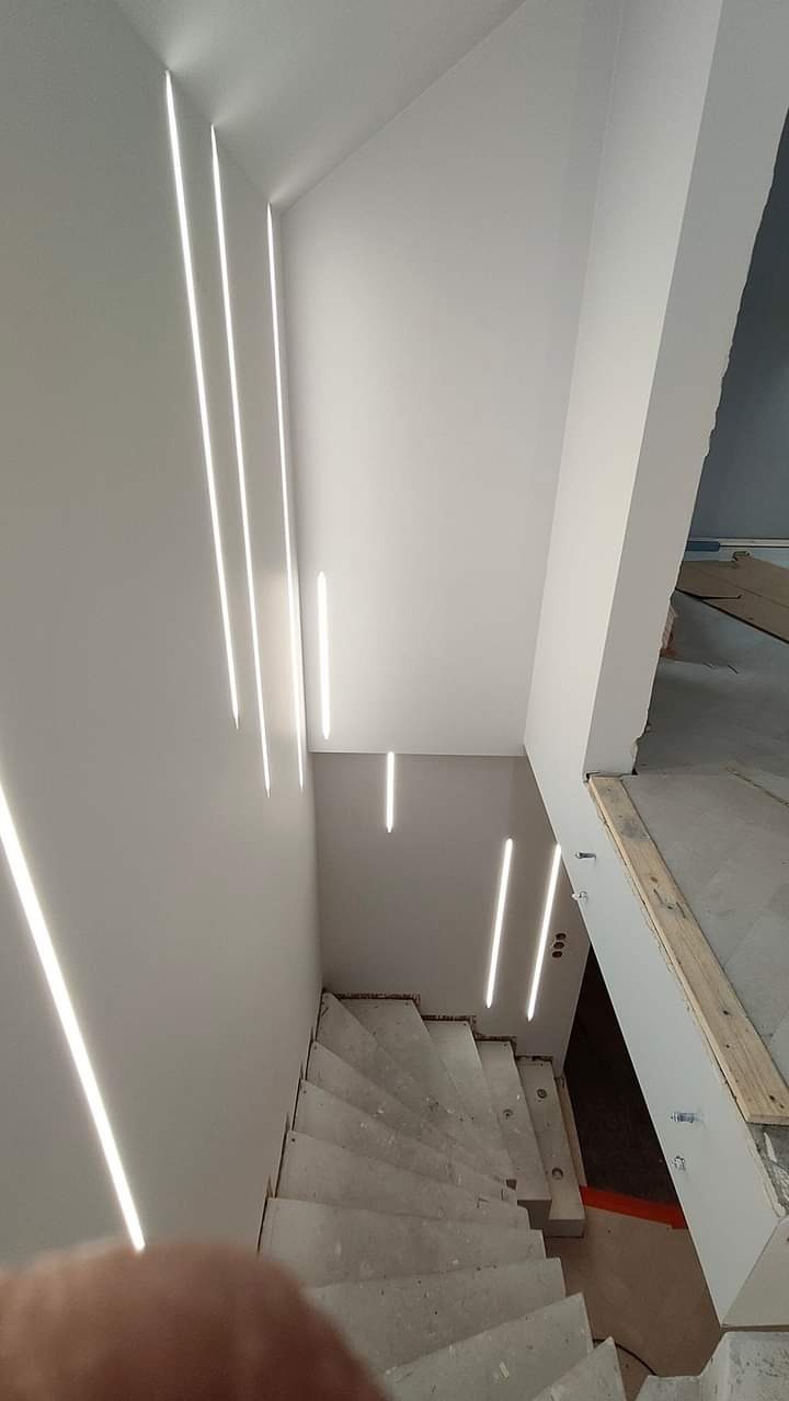 Nowoczesne oświetlenie schodów z wbudowanymi pionowymi lampami LED w ścianie, surowe betonowe schody w trakcie wykończenia.