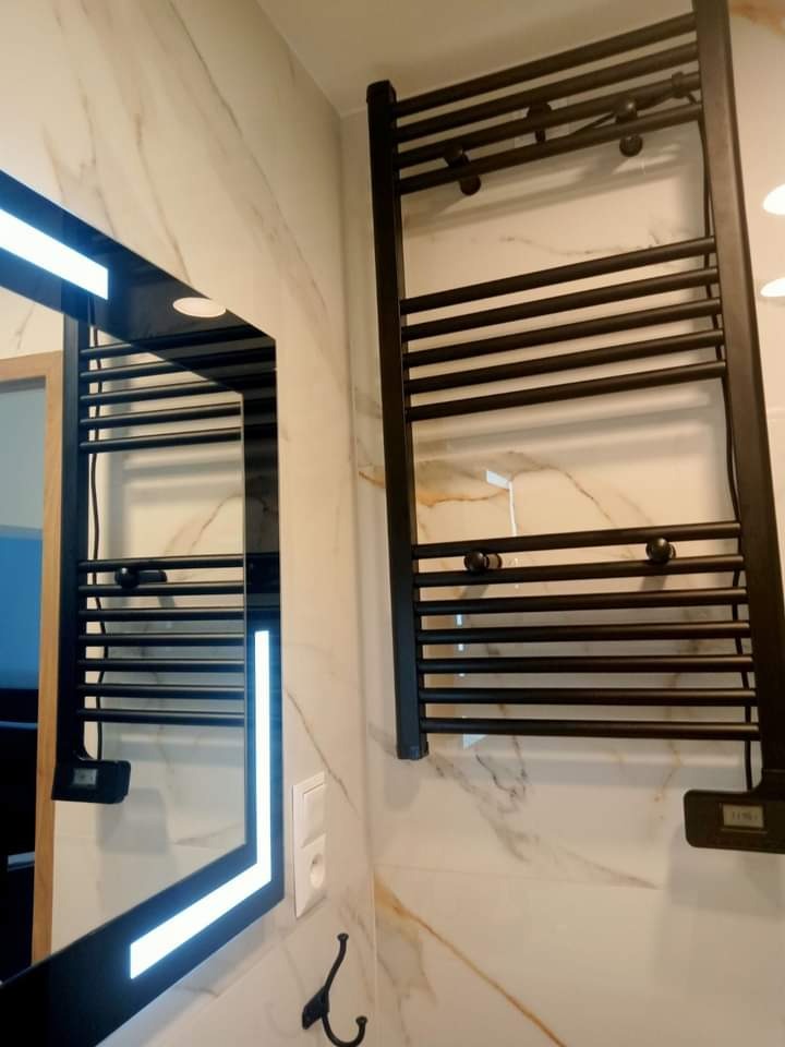 Nowoczesna łazienka z marmurowymi płytkami, czarnym grzejnikiem drabinkowym i lustrem z podświetleniem LED.