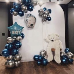 MAGIC PARTY Karolina Stolarek - Dekoracja balonowa w odcieniach niebieskiego i srebrnego z pluszowym misiem na przyjęcie z okazji narodzin syna, ustawiona na drewnianej podłodze.