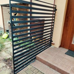 Przedsiębiorstwo Techniczne MTC Wiktor Suska - Nowoczesna, czarna, pozioma barierka ochronna z metalowych profili, zamontowana przy wejściu do domu z brązowymi drzwiami i kamiennymi schodami.